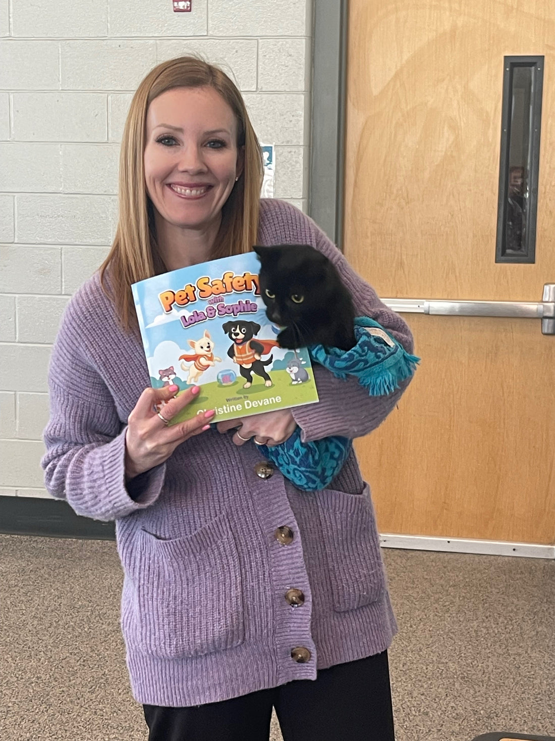Christine Devane holding Pet Safety with Lola and Sophie book alongside a black kitten at the MSPCA
