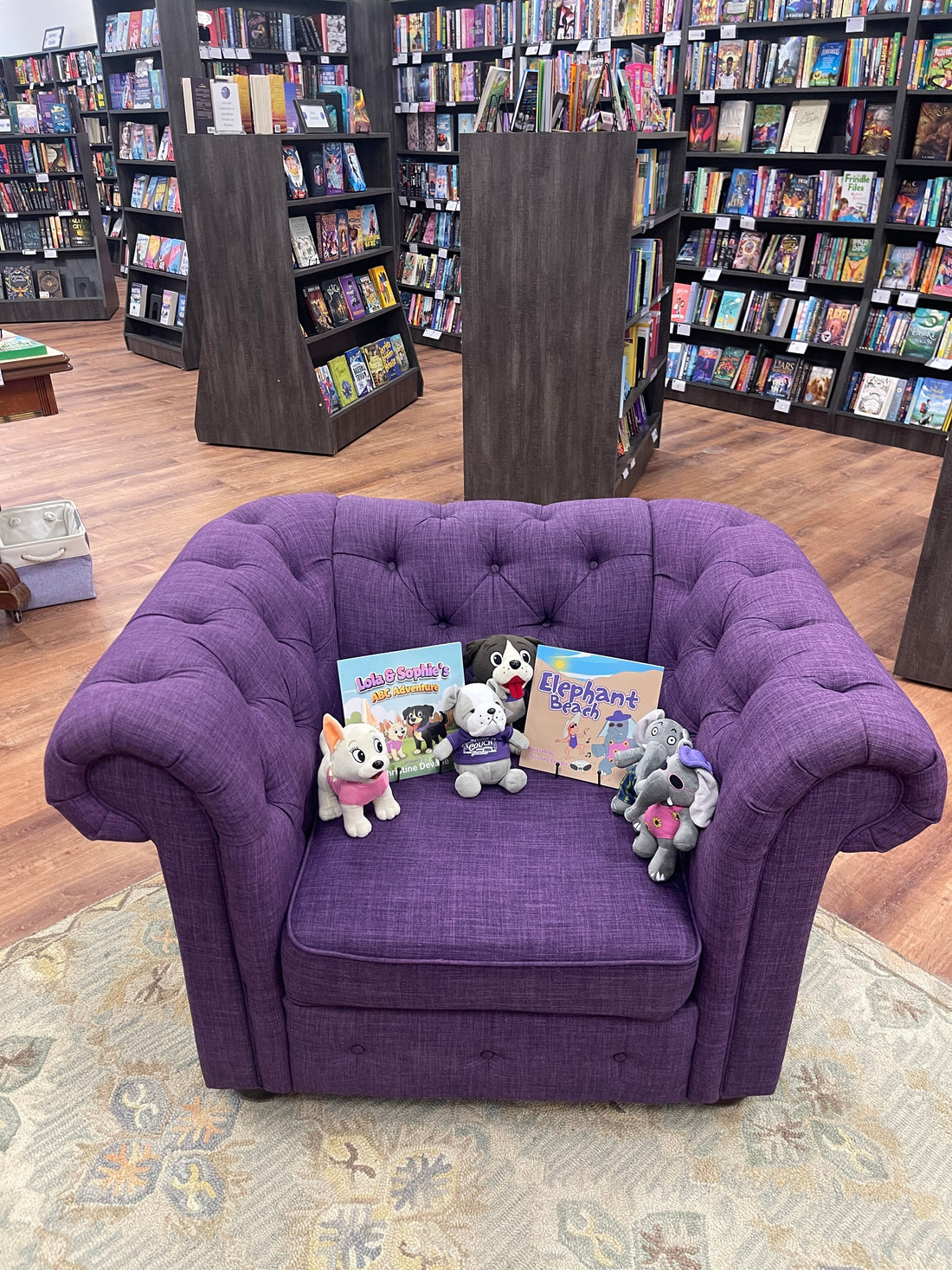 Christine Devane's books and character stuffies displayed on a purple tufted chair at The Purple Couch bookstore in North Andover