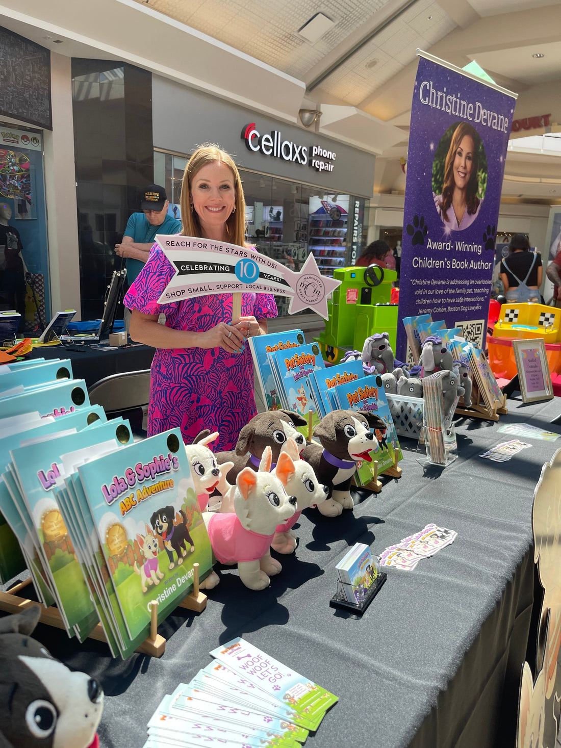 Christine Devane at her table at the Manchester Craft Market Local Author Event in NH, surrounded by her children's books and plush toys