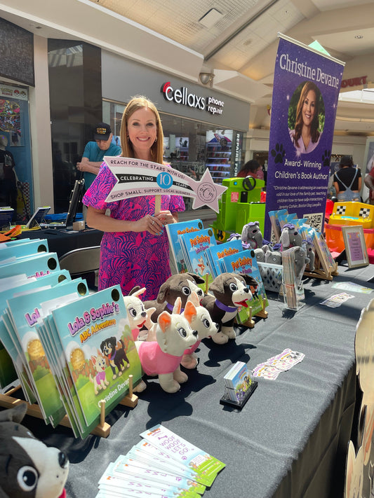 Christine Devane at her table at the Manchester Craft Market Local Author Event in NH, surrounded by her children's books and plush toys