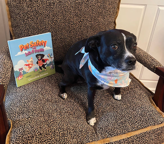 Sophie the dog sitting on a chair next to Pet Safety with Lola and Sophie book, wearing an Easter bandana