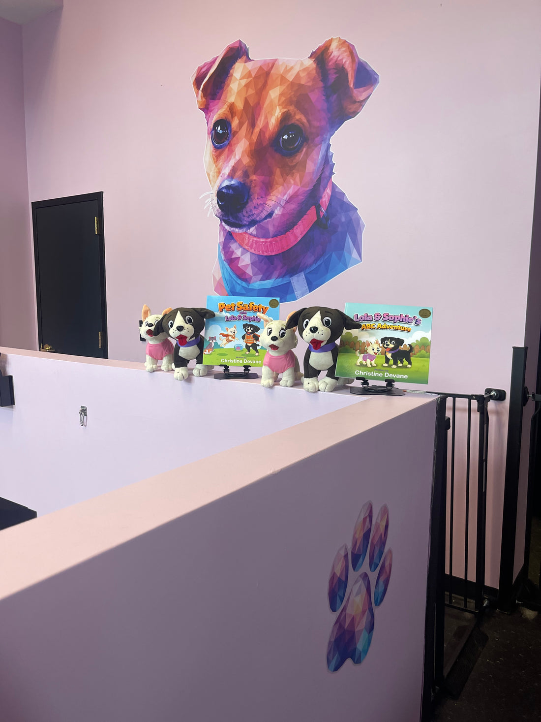 Lola & Sophie books and plush dogs displayed beneath a colorful dog portrait at Latte’s Landing in Billerica.